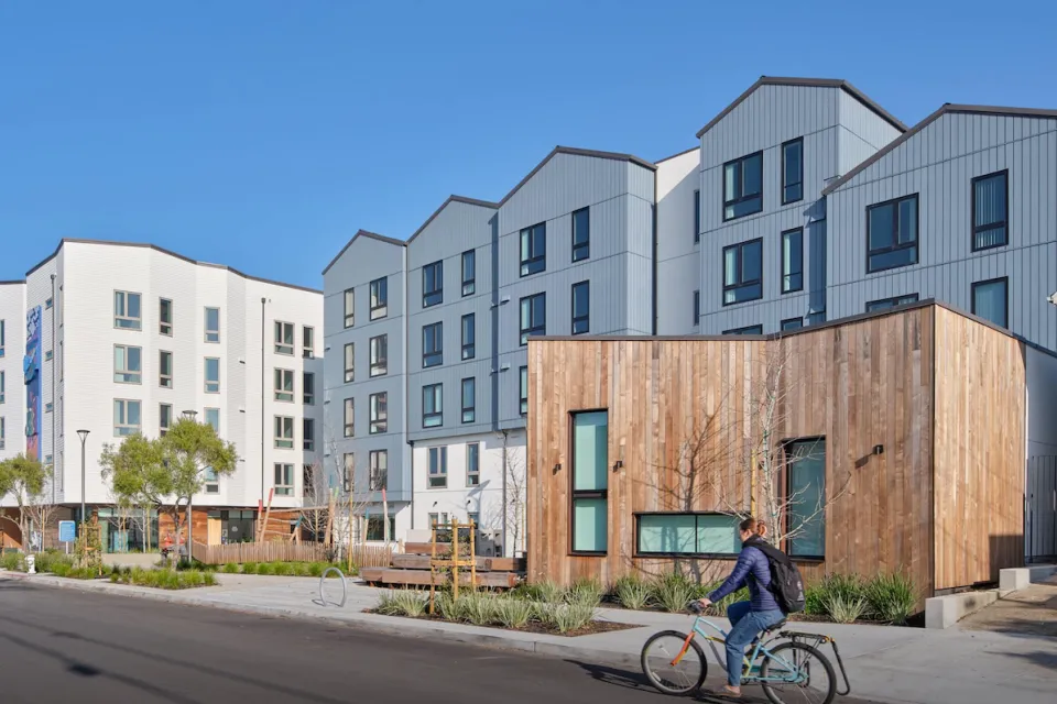 Rendering of Shirley Chisholm Village four-story housing development with person biking in front.